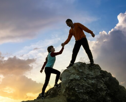 A man and woman are shaking hands on top of a rock.