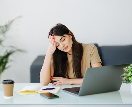 A woman sitting at a desk with her head resting on one hand.