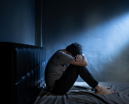 A man sitting on the bed with his head down.